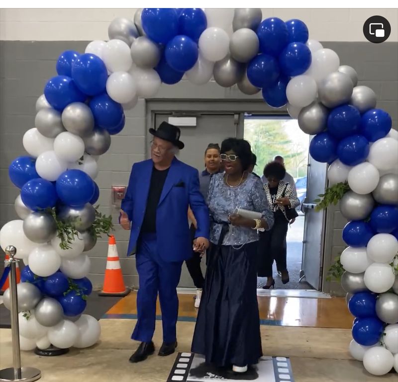 Couple walking through a blue, white and silver balloon arch entrance