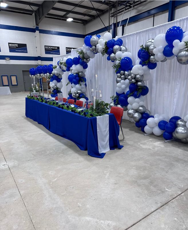 Long banquet table with blue linens, balloon archway and candle centerpieces